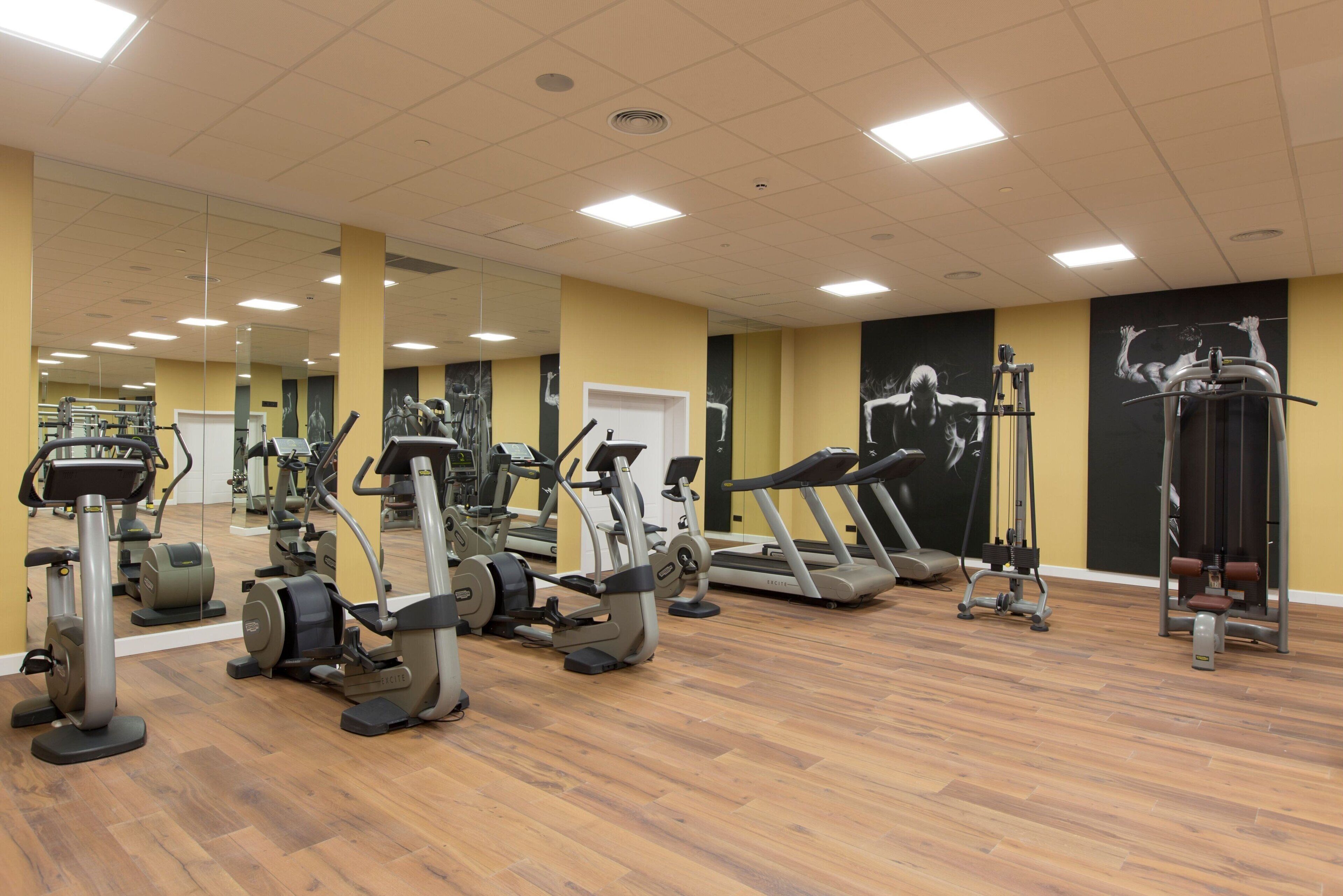A gym with various exercise equipment, mirrors, and a wooden floor.