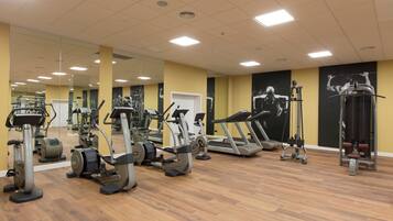 Een sportschool met diverse fitnessapparaten, spiegels en een houten vloer.