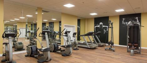 A gym with various exercise equipment, mirrors, and a wooden floor.