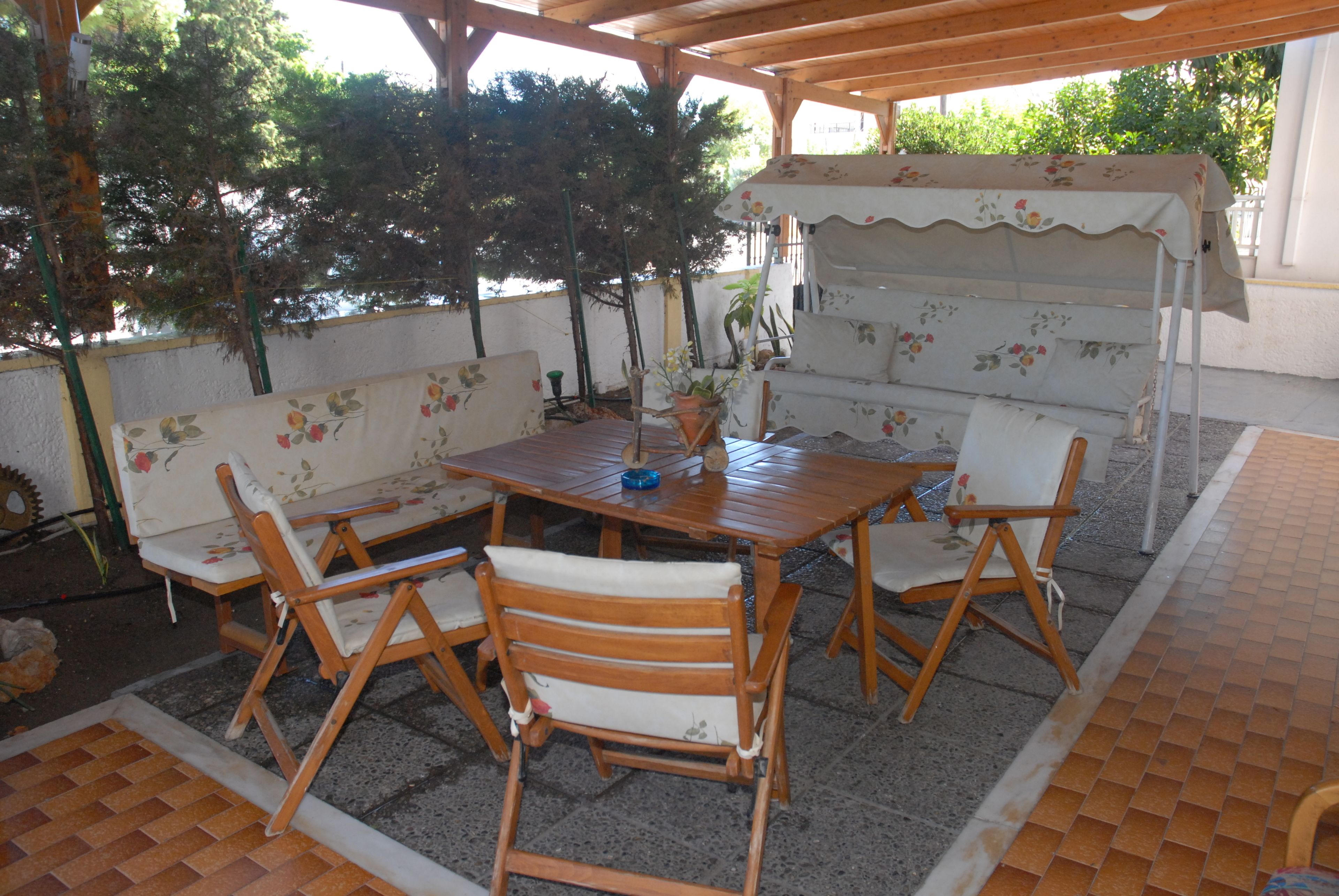 Un patio exterior con una mesa y sillas de madera, un sofá floral y una zona de estar cubierta.