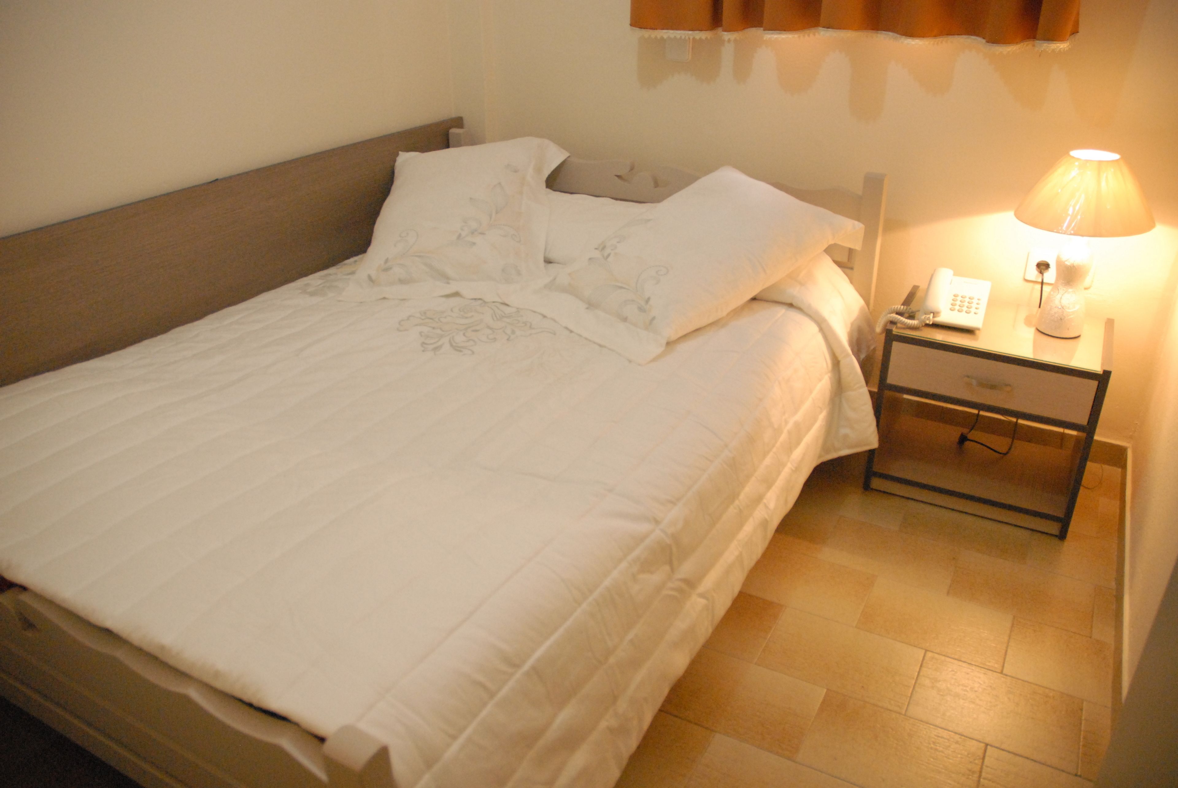 Un lit bien fait, avec une couette blanche et des oreillers, une table de chevet avec une lampe et un téléphone.