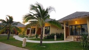 Un resort con villas de techo de paja, palmeras y un césped cuidado.