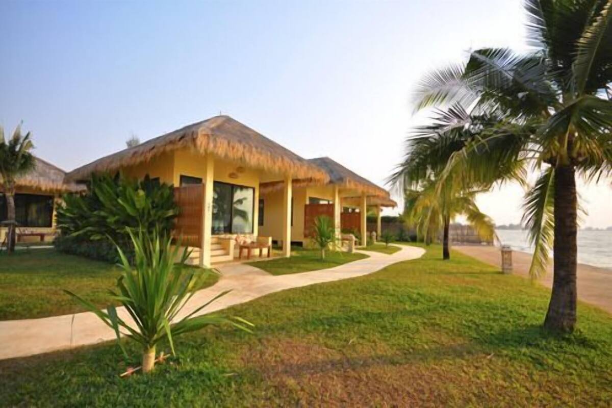 A resort with thatched-roof cabins, a well-maintained lawn, and a pathway leading to the beach.