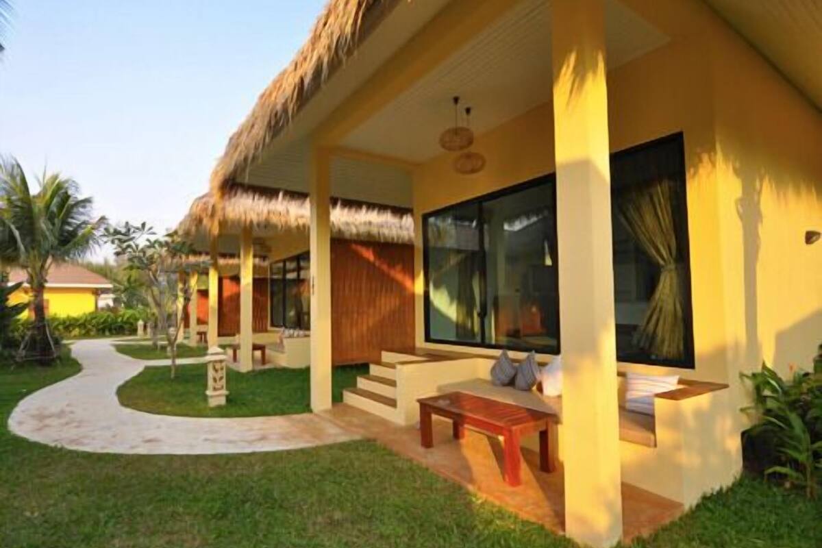 A resort with a thatched roof, a covered outdoor seating area, and a pathway leading to the entrance.