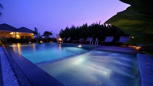 Una piscina al anochecer con sillones de descanso y un edificio al fondo.