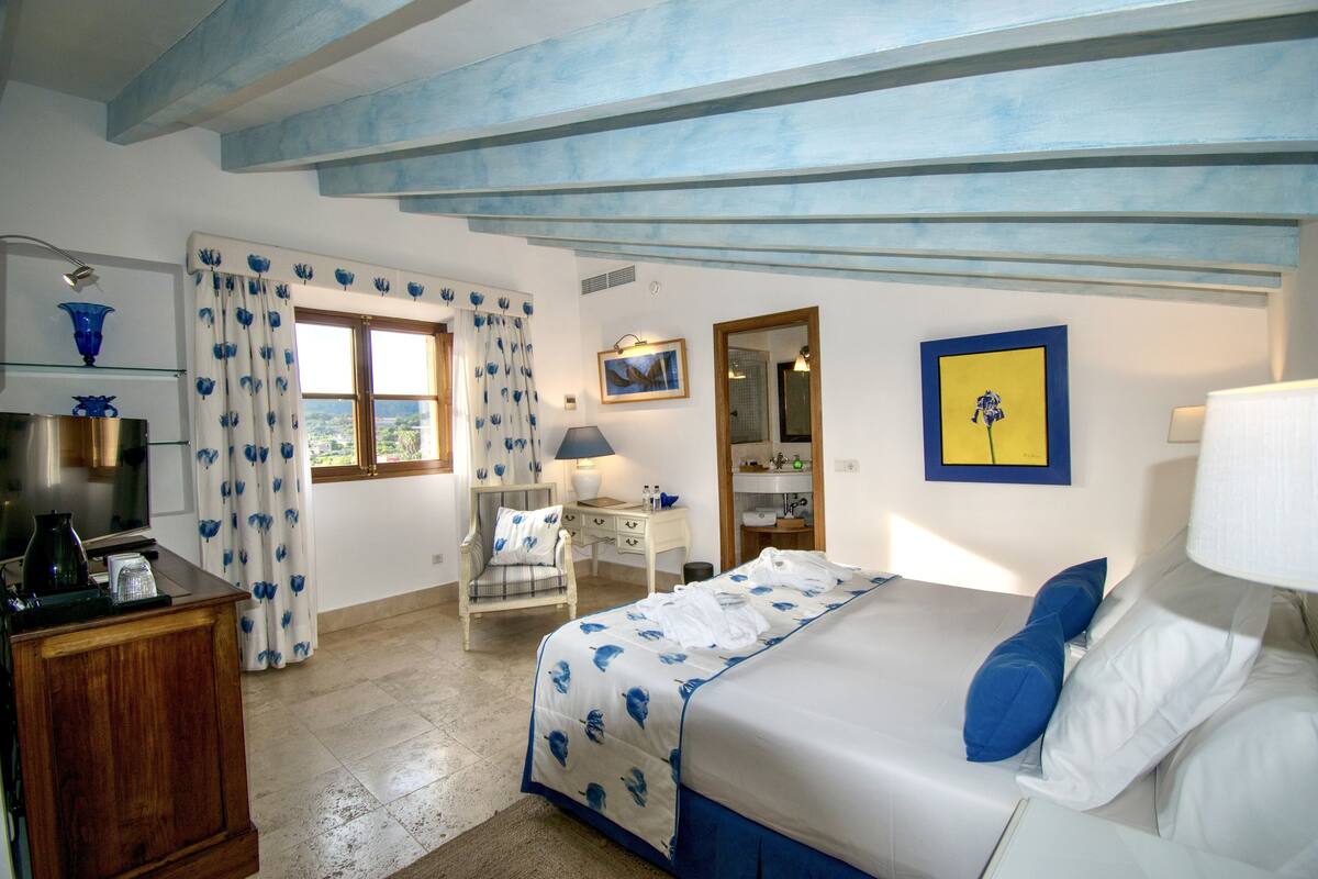 A bedroom with a bed, a desk, a chair, a TV, and a bathroom visible through an open door.