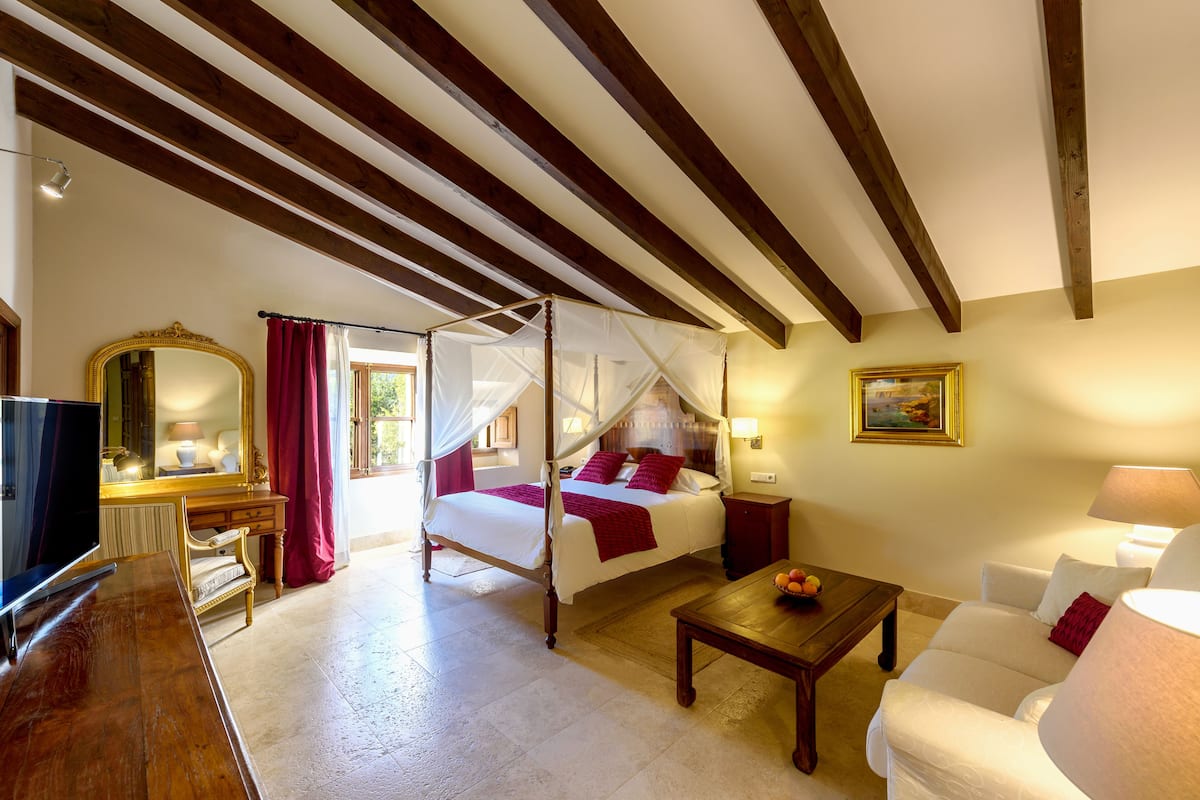 A bedroom with a four-poster bed, a television, a desk, and a sofa.