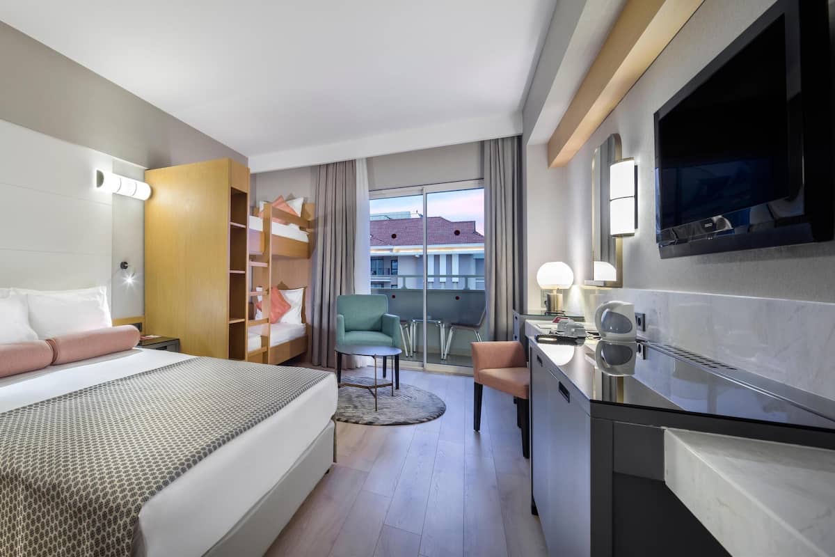 A hotel room with a bed, bedside table, lamp, TV, and a view of the city.