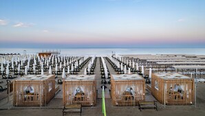 Ein Strandhotel mit Reihen von Liegestühlen und Sonnenschirmen, Holzhütten und Blick auf den Ozean.
