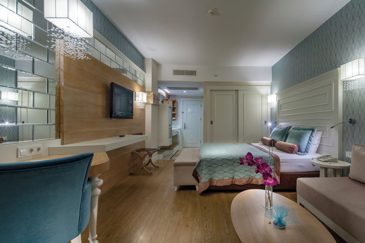 Habitación de hotel moderna con una cama grande, un sofá, un televisor y un espejo.