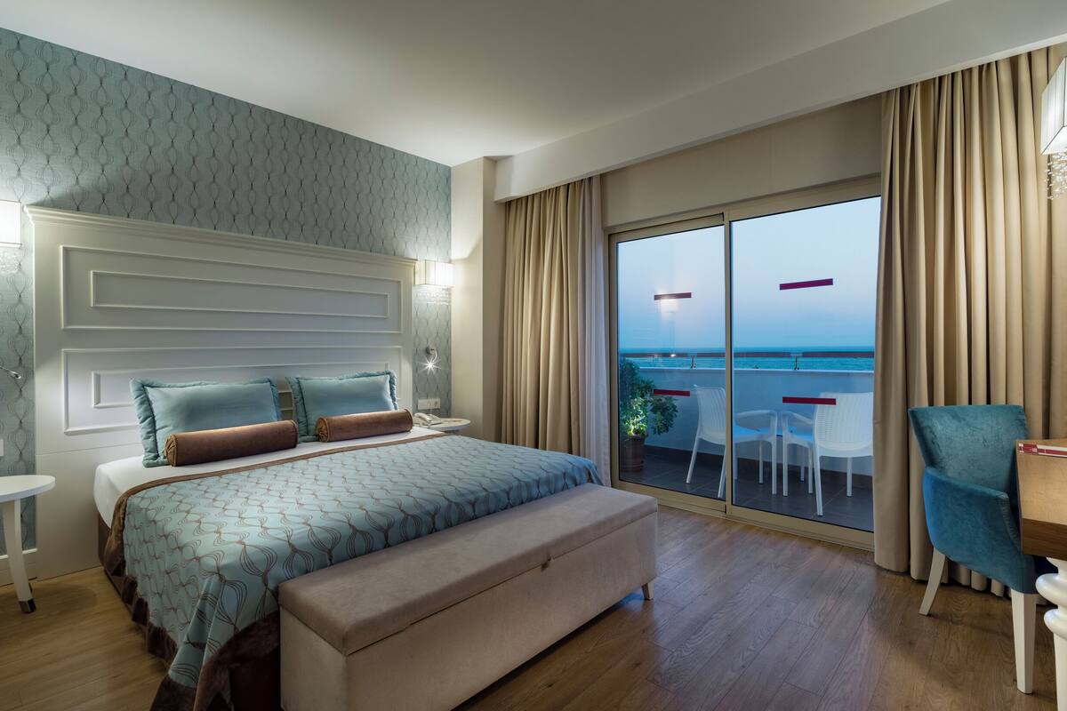 Habitación de hotel con cama, escritorio, silla, una mesita y vistas al mar a través de un ventanal grande.