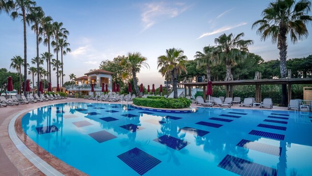 A swimming pool with lounge chairs and umbrellas, surrounded by palm trees. - Trendy Palm Beach (Adults Only, 16+) - All inclusive (Manavgat)