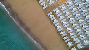 Vue aérienne d’une plage bordée de rangées de transats blancs et de parasols.