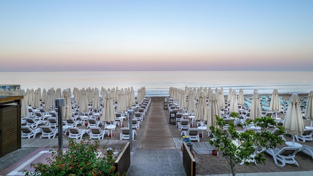 A beachside resort with rows of sun loungers and umbrellas, a wooden walkway leading to the beach, and a clear view of the ocean. - Trendy Side Beach (Adults Only, 16+) - All inclusive (Manavgat)