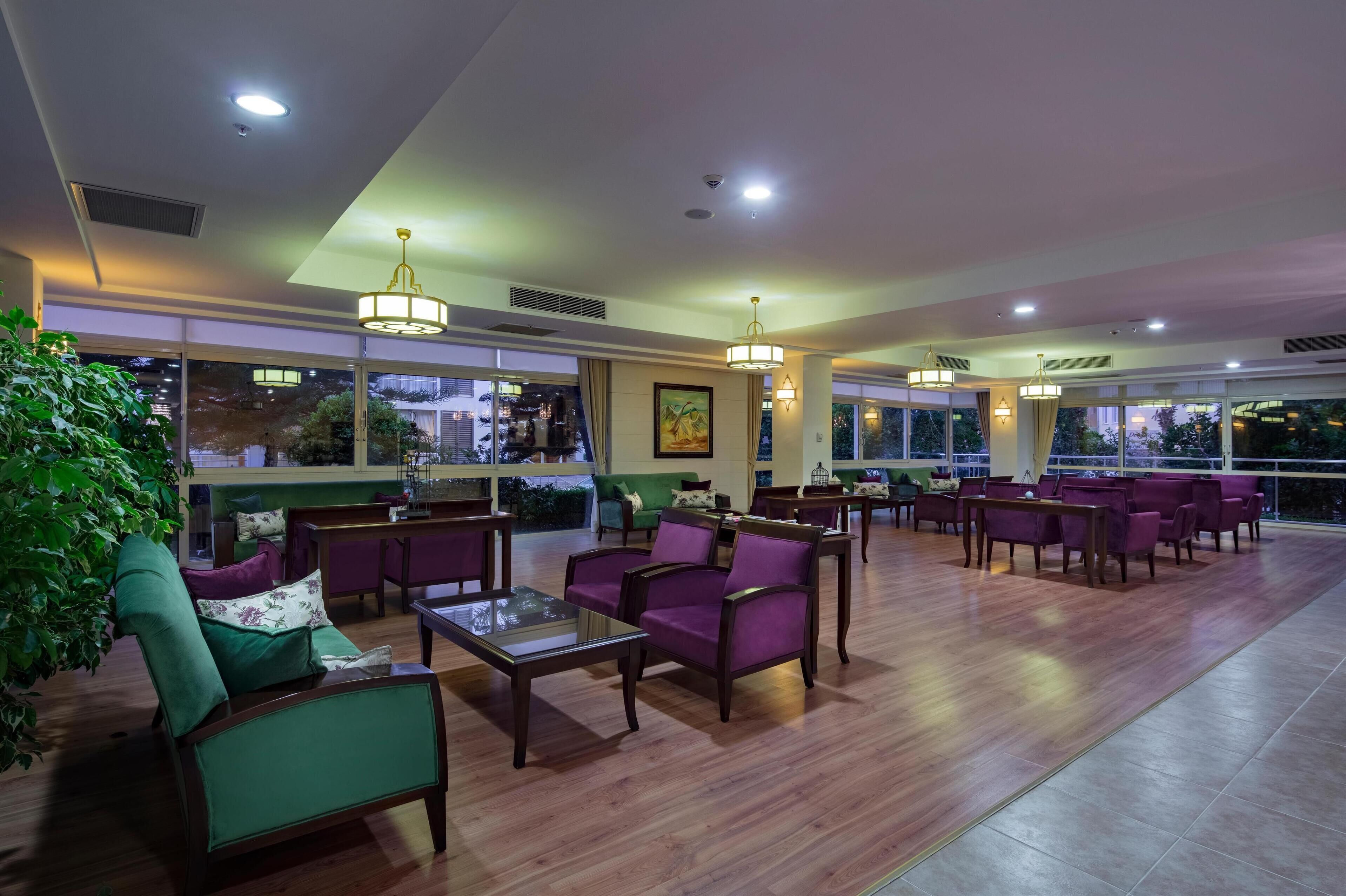A spacious lobby with wooden flooring, purple and green seating, large windows, and multiple ceiling lights.