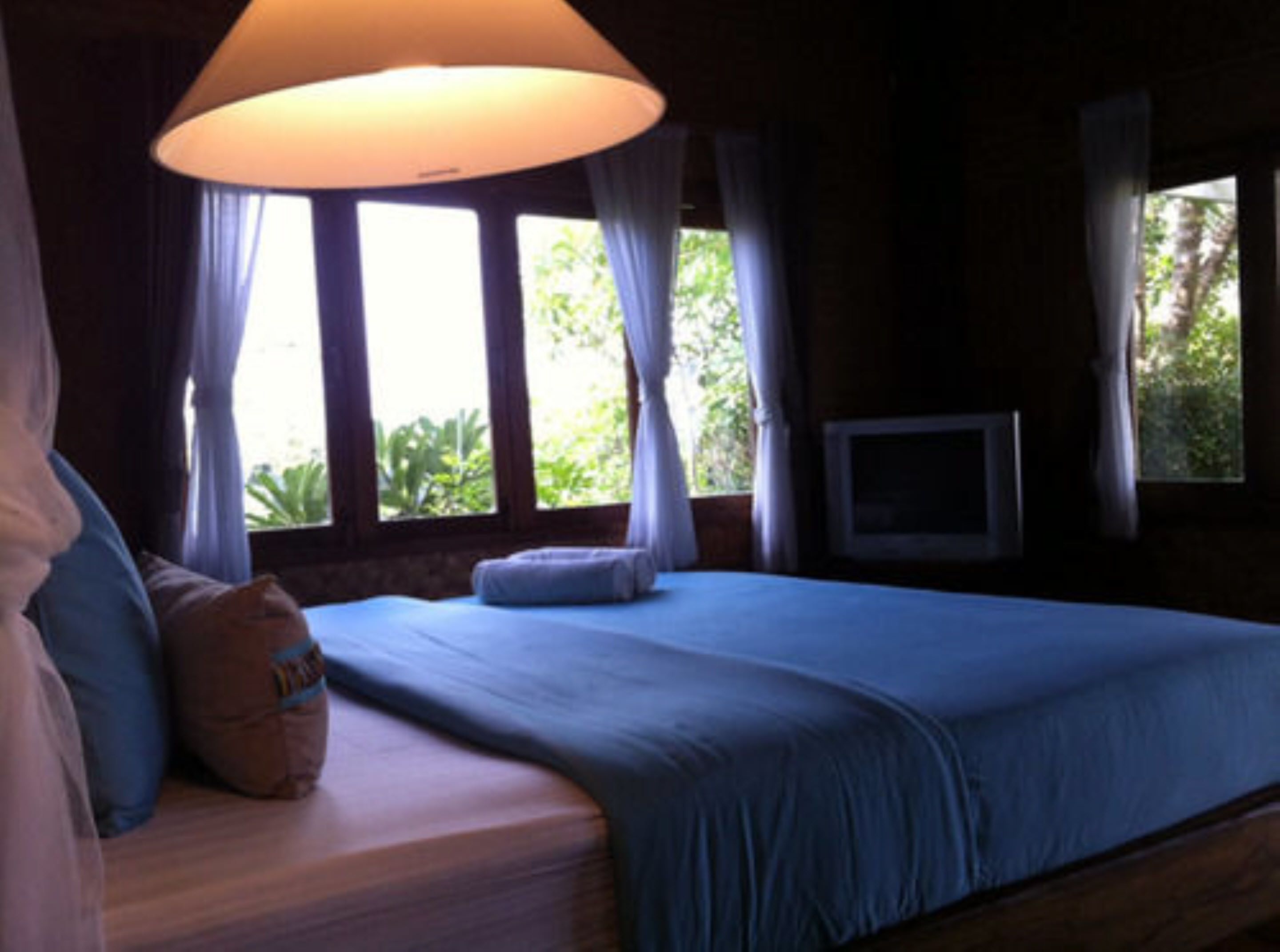 A bedroom with a large bed, a television on the wall, and windows with curtains.