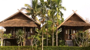 Two thatched-roof cottages with a staircase leading to a covered porch, surrounded by tropical vegetation. - Vimarnkiri Resort (Pai)