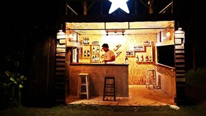 A small outdoor bar with a star decoration above the counter, wooden shelves with bottles, and a ladder. - Vimarnkiri Resort (Pai)