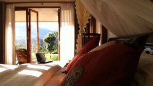 A bedroom with a bed, a laptop on a table, and a view of the outdoors through a window. - Vimarnkiri Resort (Pai)