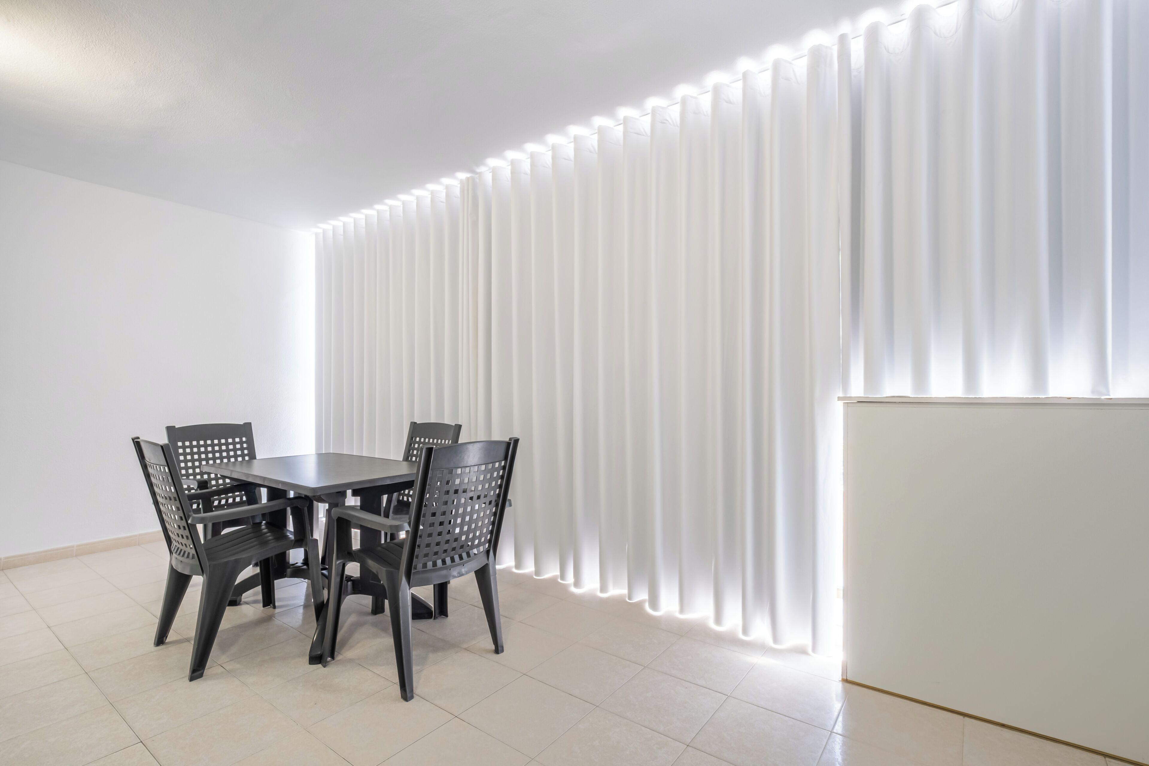 Un comedor con una mesa y sillas, una pared blanca y una cortina con líneas verticales.