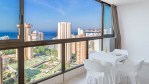 A high-rise apartment with a large window offering a city view, a dining area with white furniture, and a small table with a glass of juice. - Apartamentos Gemelos 2 - Beninter (Benidorm)