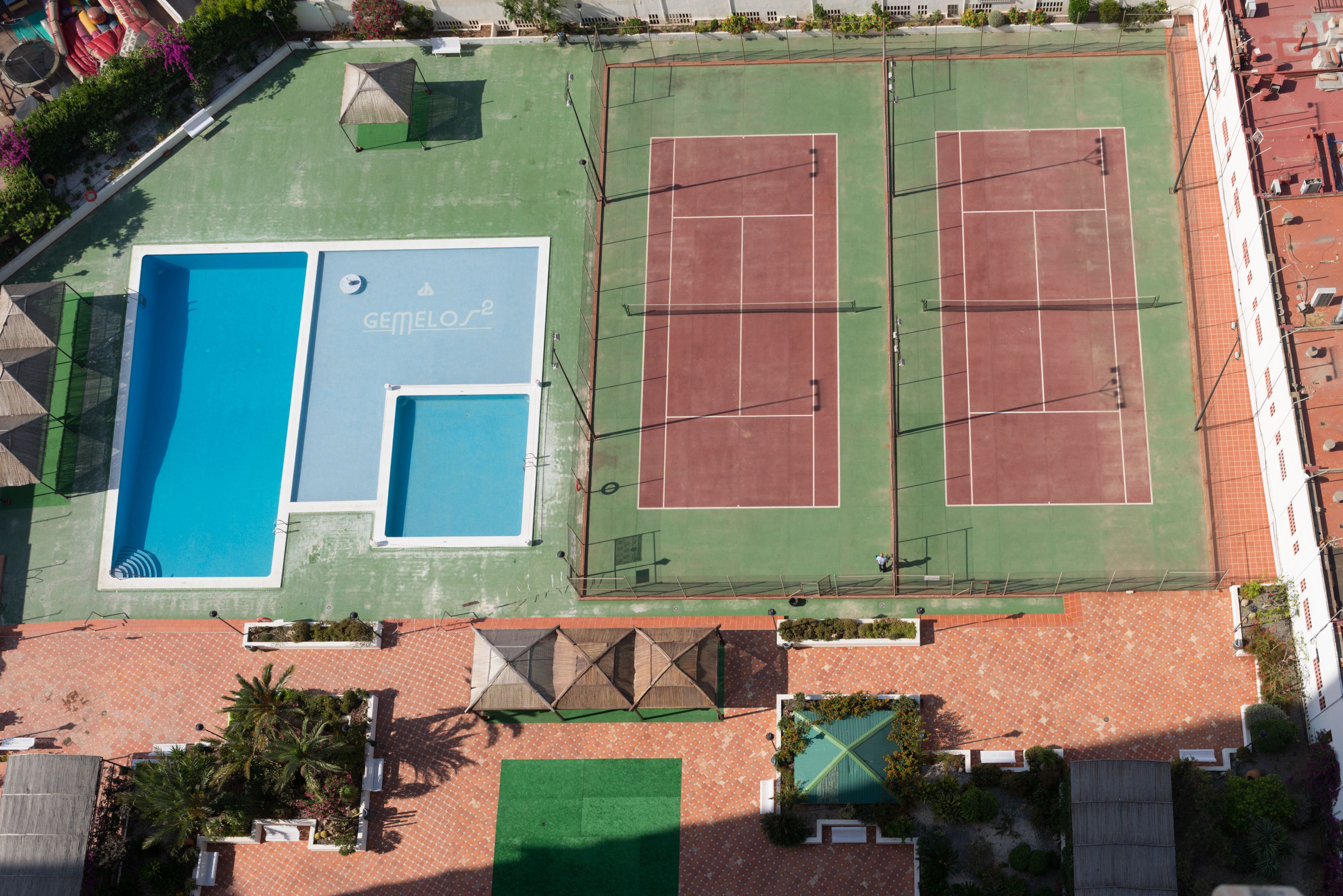 Tagterrasse med swimmingpool, tennisbaner og en lille have.