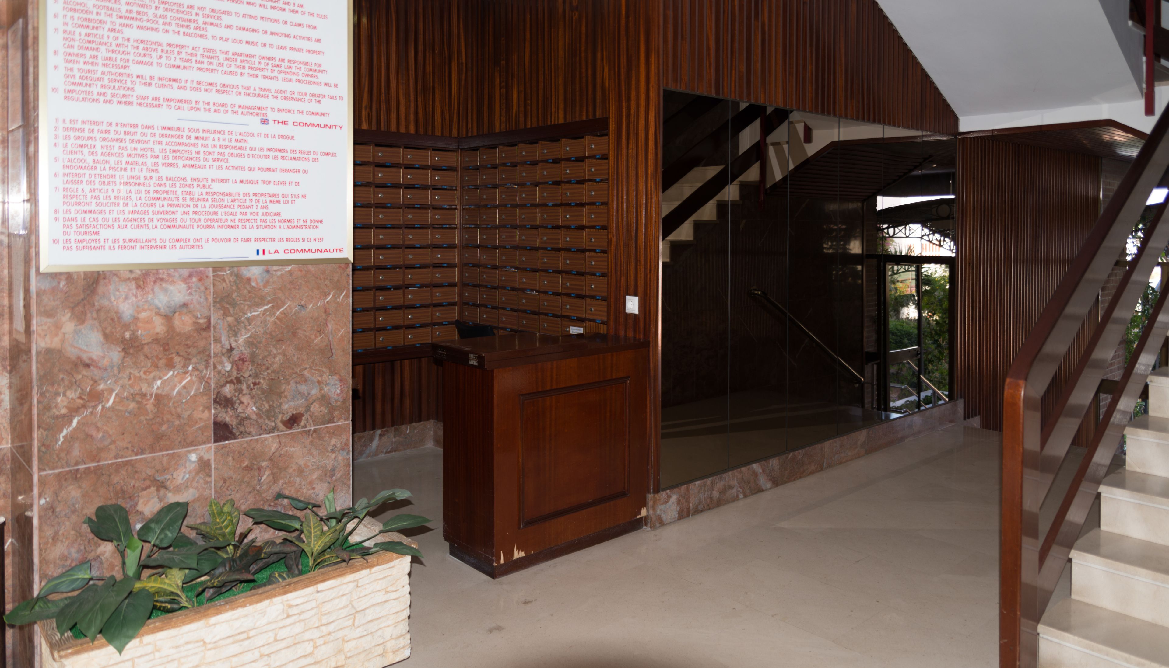 A modern interior with a wooden reception desk, a marble wall, and a staircase leading to upper floors.