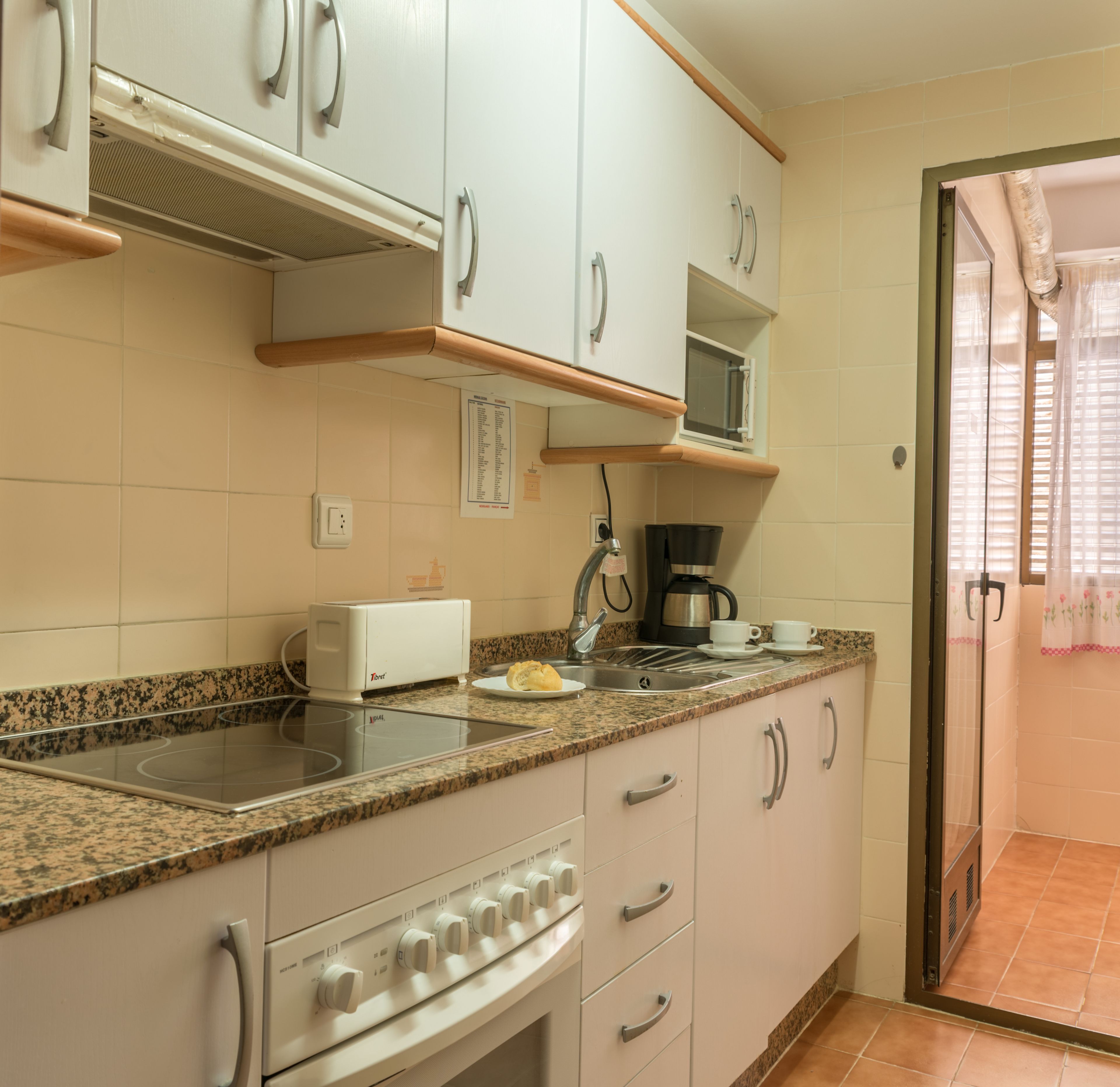 Una cocina con gabinetes blancos, encimera de granito, estufa, microondas y cafetera.