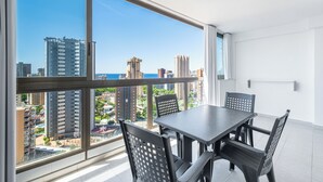 A balcony with a table and chairs, large windows with a city view, and a white interior. - Apartamentos Gemelos 2 - Beninter (Benidorm)