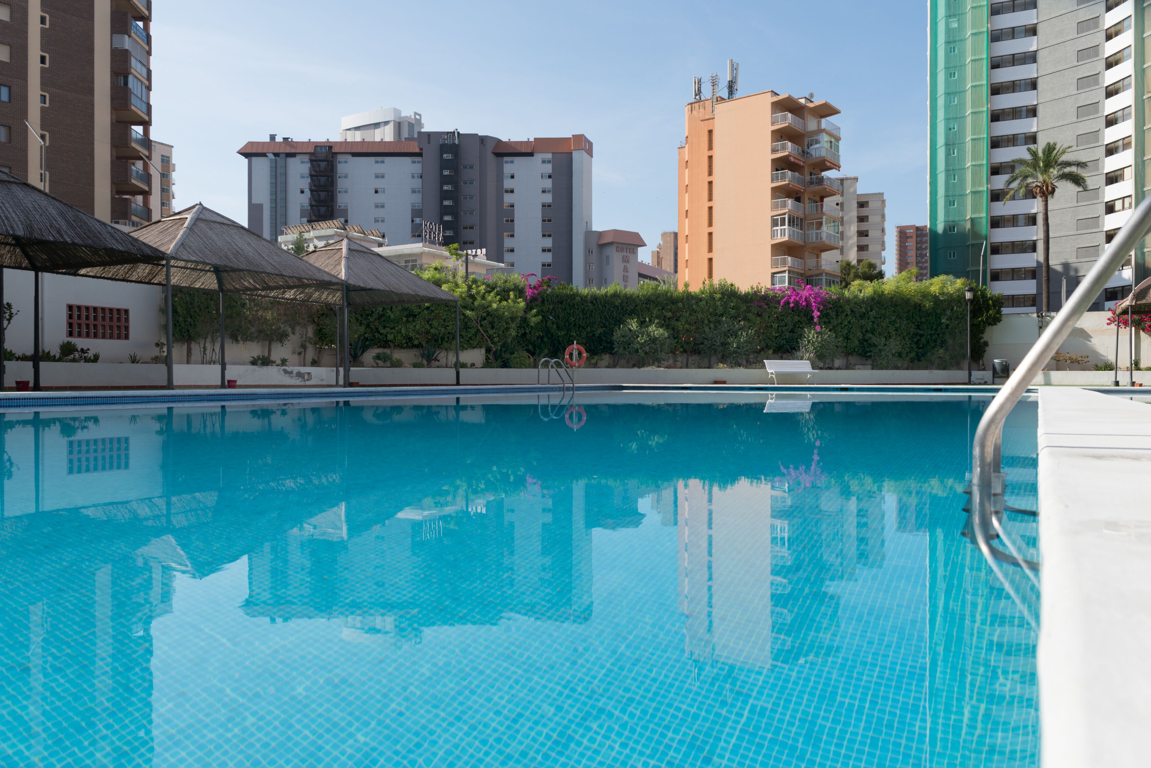 A swimming pool with a clear blue water surface, surrounded by high-rise buildings, some with balconies.