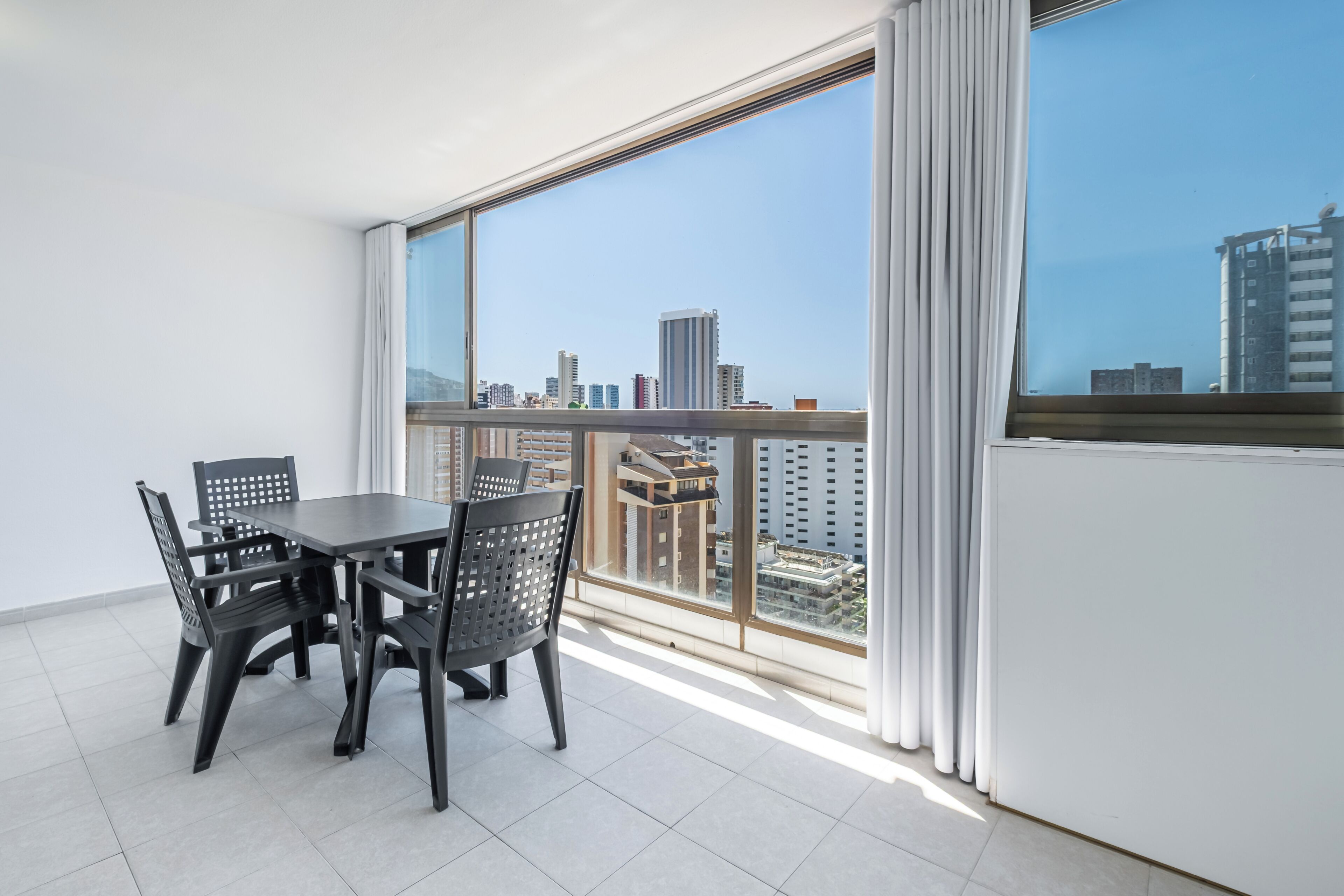 A balcony with a table and chairs, a view of a cityscape, and a large window with curtains.