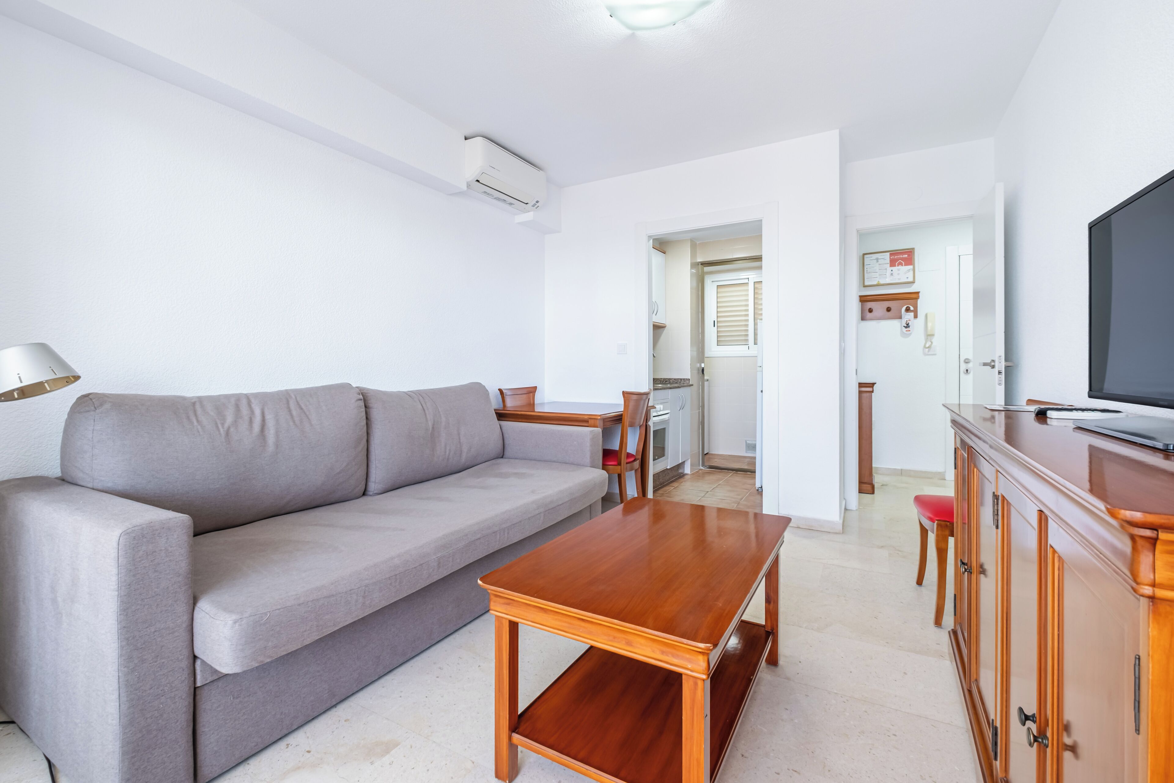A living room with a sofa, a wooden coffee table, a TV, and a kitchen area in the background.