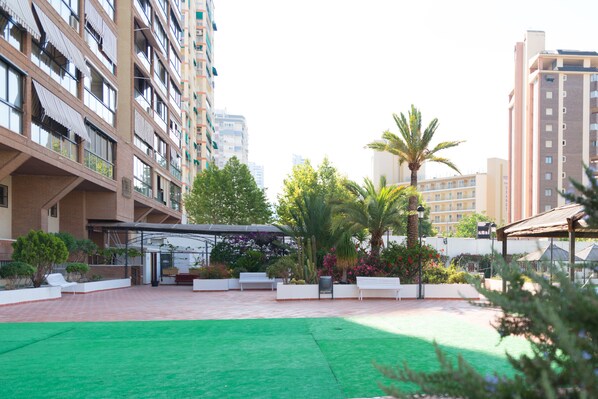 A courtyard with a green lawn, white benches, and potted plants.
