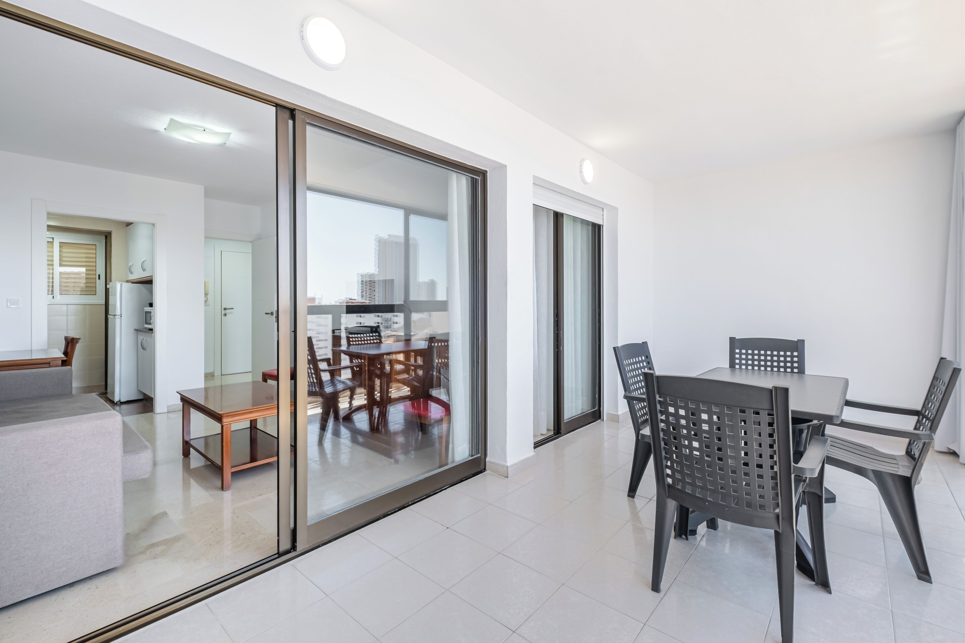 A modern apartment with a dining area, kitchenette, and a view of the city through a glass door.