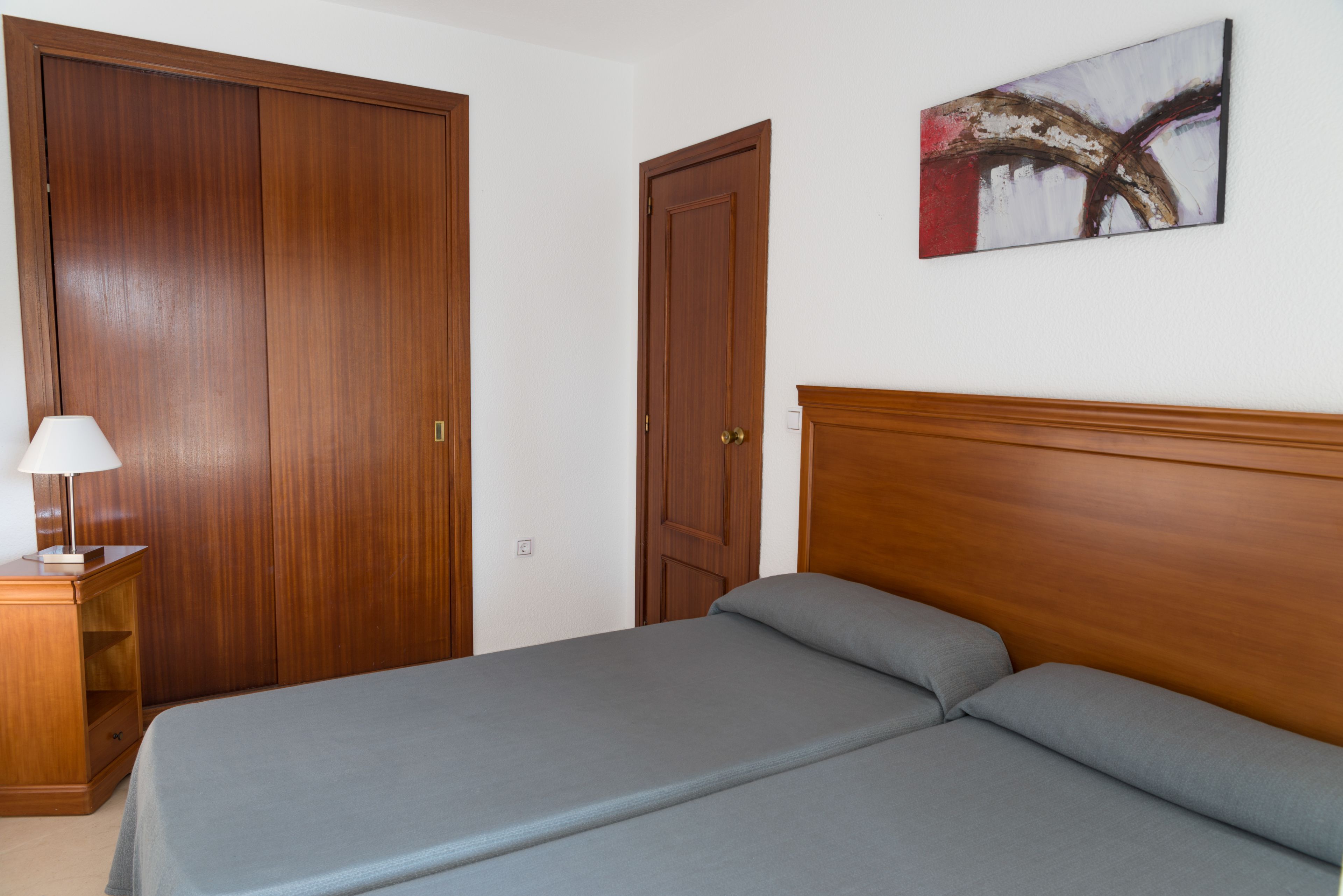 A bedroom with a bed, a nightstand with a lamp, and two wooden doors.