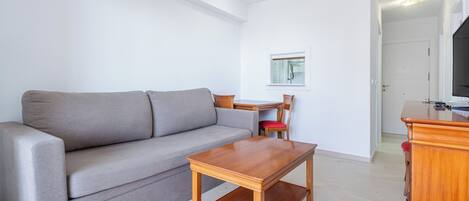Un salón con un sofá gris, una mesa de centro de madera, un mueble para televisor y una ventana con persianas.