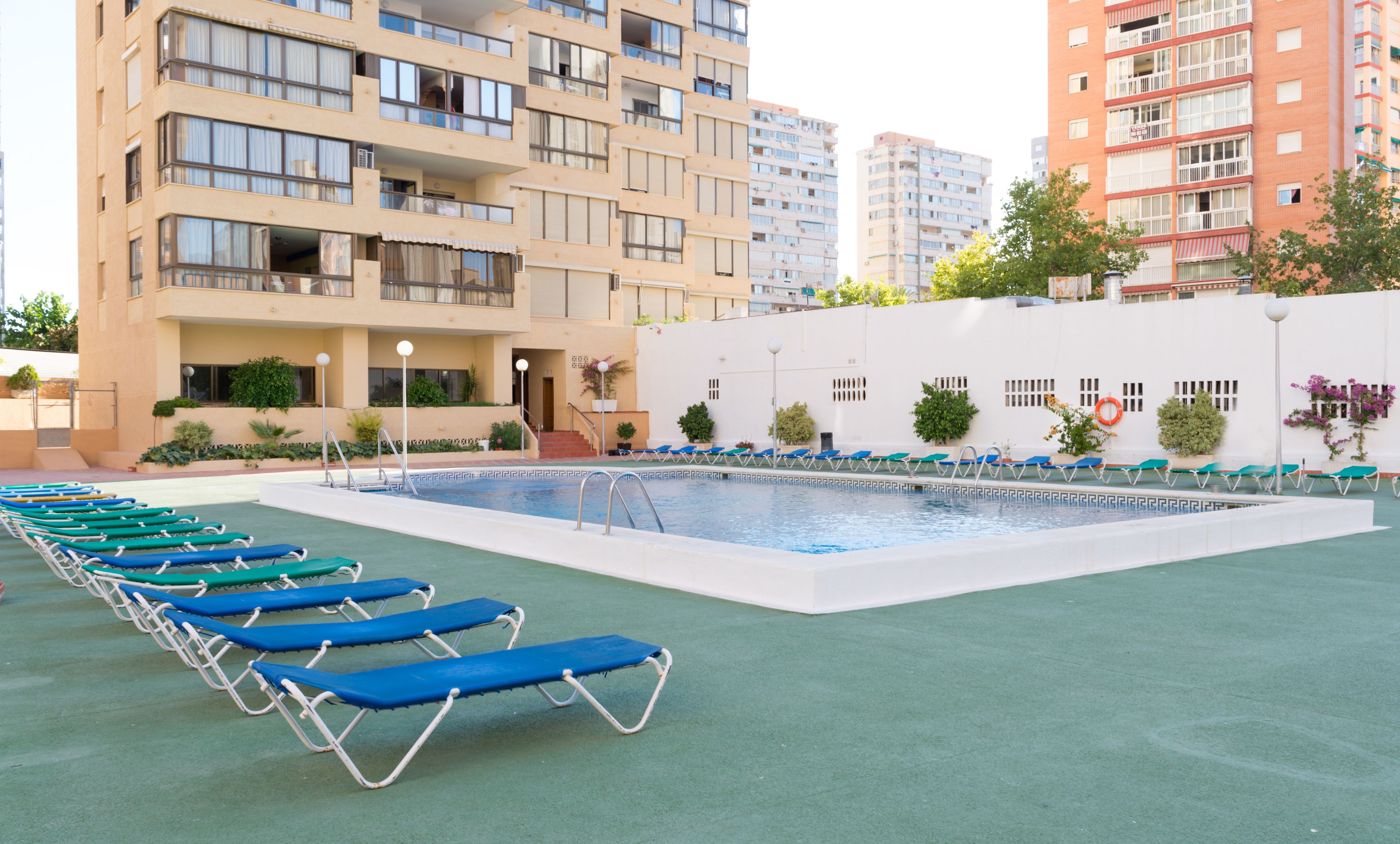 A swimming pool with lounge chairs, surrounded by a building with multiple balconies and windows.