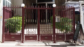 Entrada de un edificio con una reja metálica, un letrero sobre la reja y un cartel pequeño en la acera.