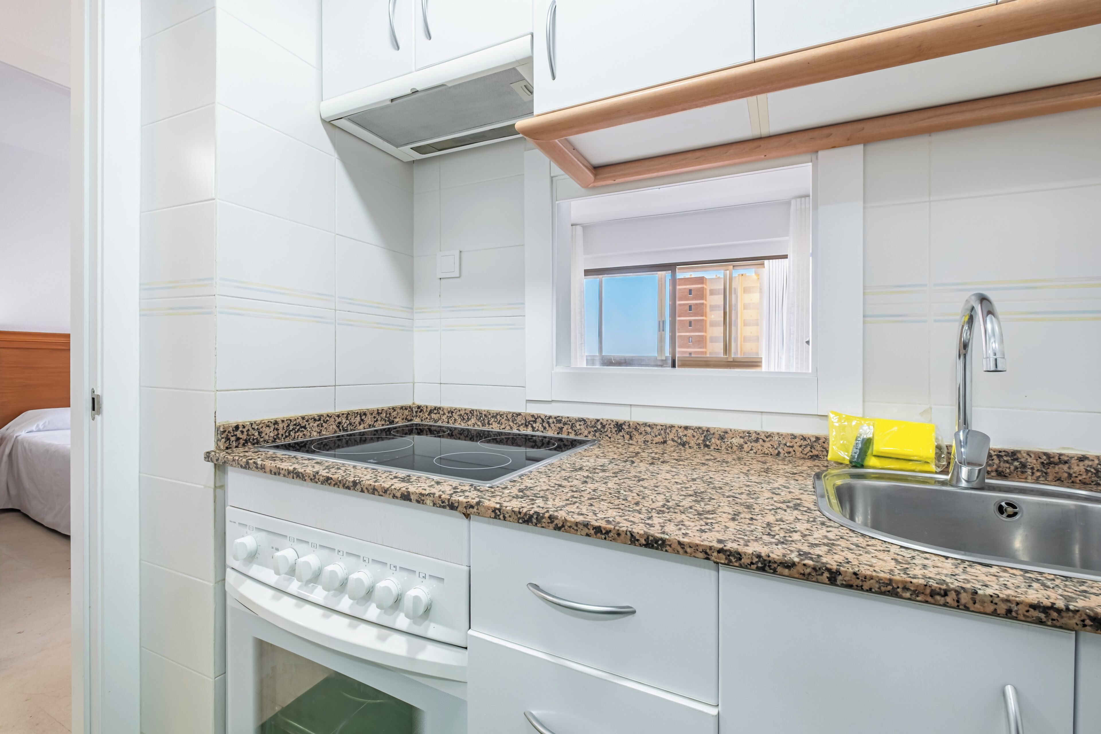 A kitchen with white cabinets, a granite countertop, a stainless steel sink, and a window above the sink.