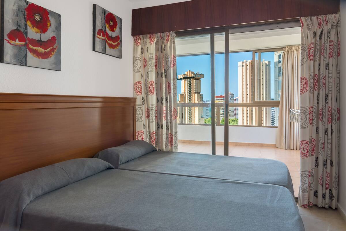 Ein Hotelzimmer mit einem großen Bett, einem Holzkopfende und einem Balkon mit Vorhängen.