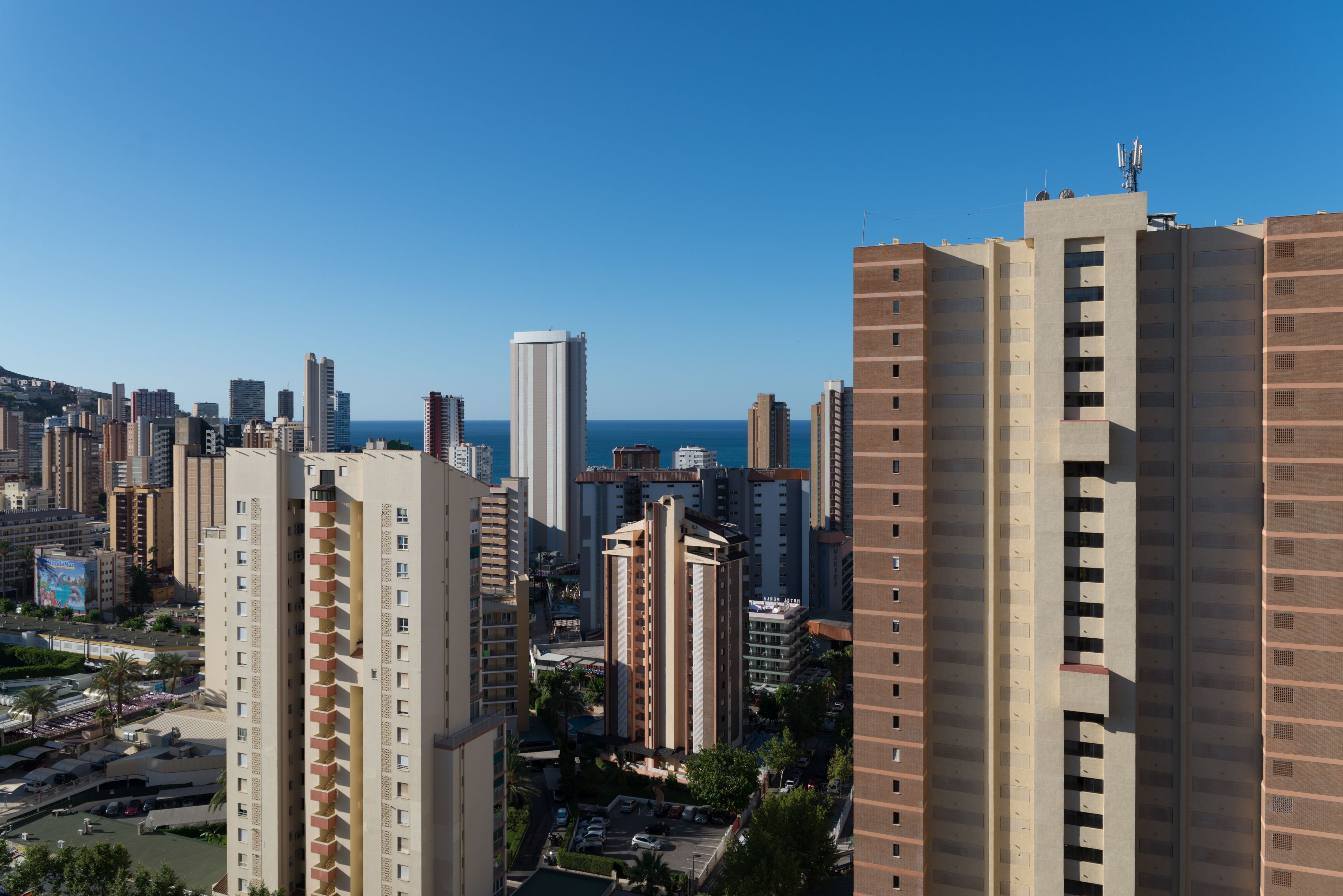 A high-rise building with multiple floors, balconies, and a clear view of the sea in the background.