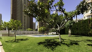 Un patio con césped y una pequeña piscina, rodeado de árboles y edificios altos.