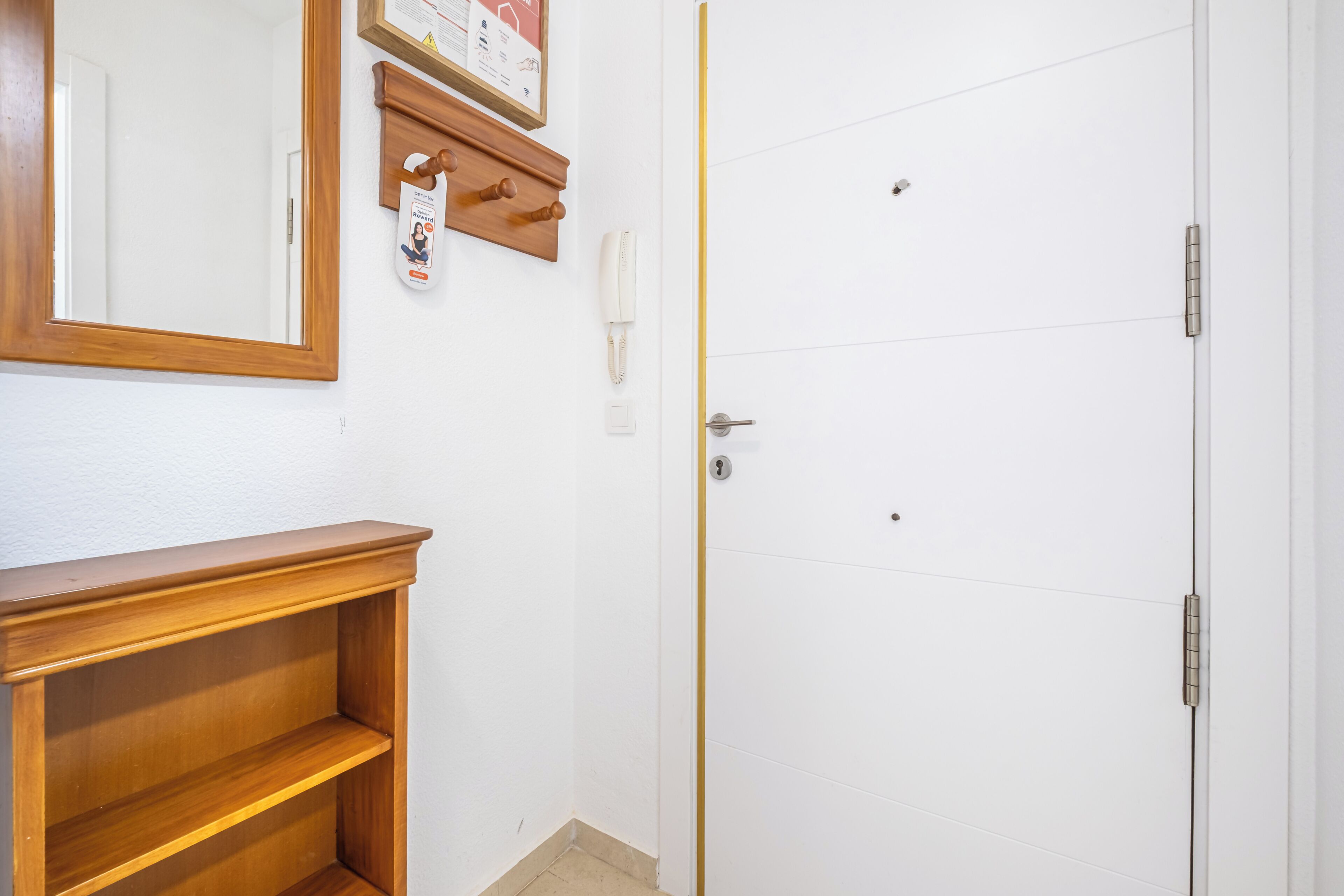 A white door with a keyhole and a lock, a wooden shelf, a wall-mounted telephone, and a framed certificate or notice.