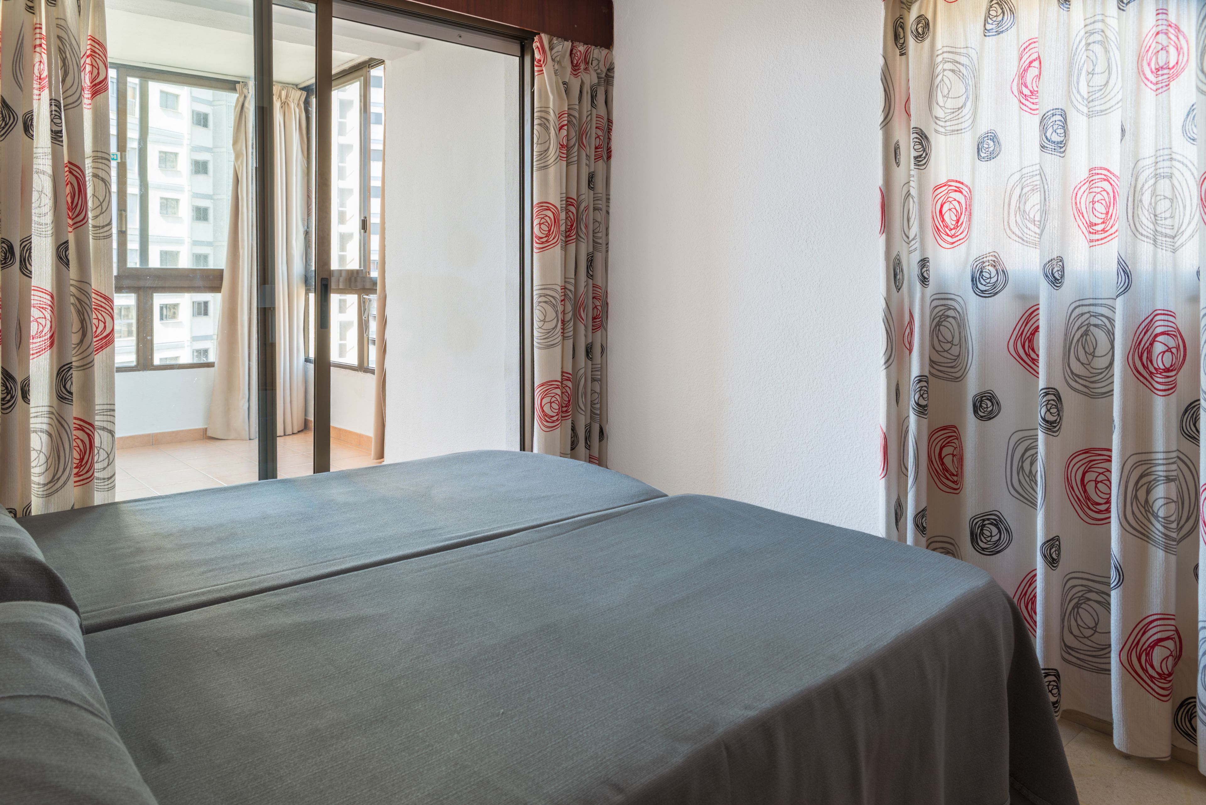 Quarto de hotel com cama, vista de um edifício pela janela e cortinas estampadas.