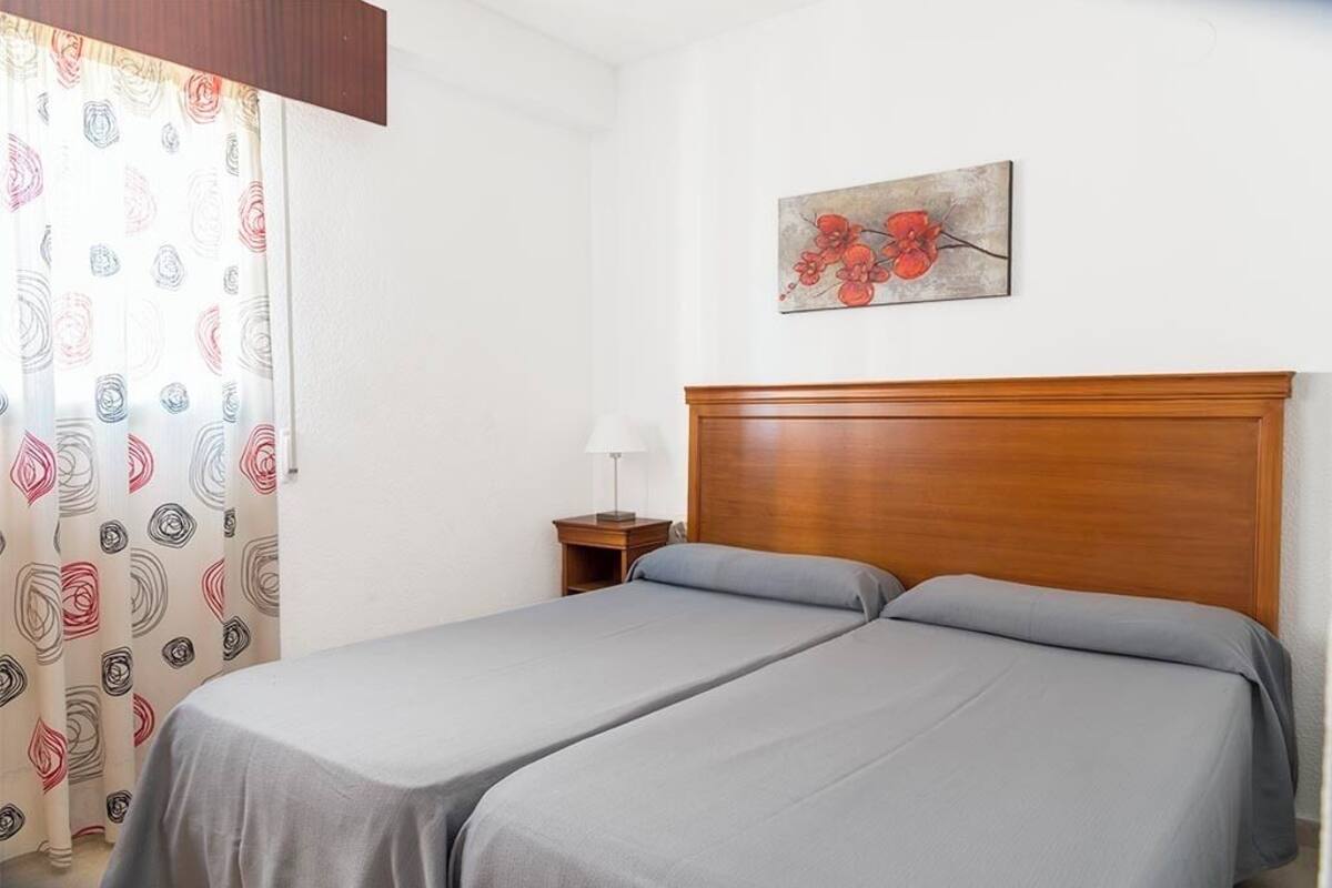 Ein Hotelzimmer mit zwei Betten, einem Holz-Kopfteil, einem Nachttisch mit Lampe und einem floralen Kunstwerk an der Wand.
