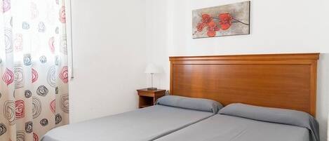 Et hotelværelse med to senge, et trægavl, et natbord med en lampe og et blomsterbillede på væggen.