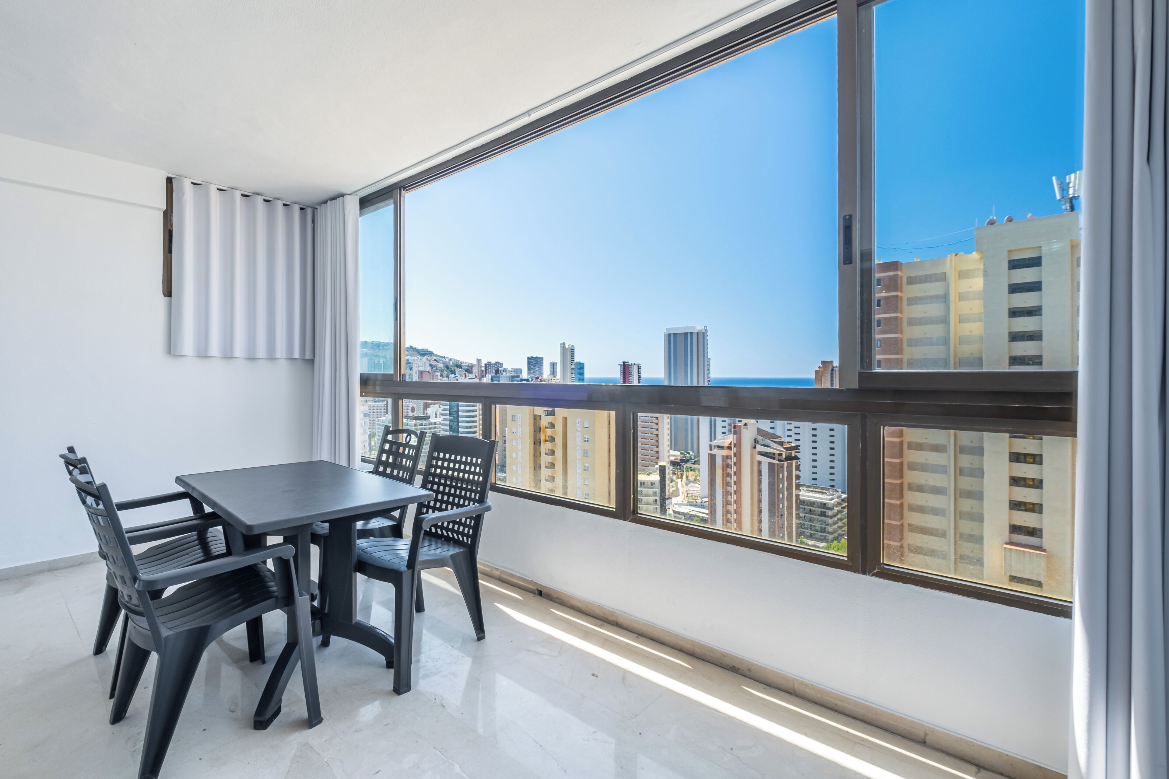 A balcony with a city view, a table with chairs, and a window with blinds.