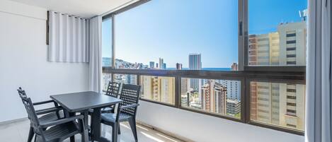 A balcony with a city view, a table with chairs, and a window with blinds.