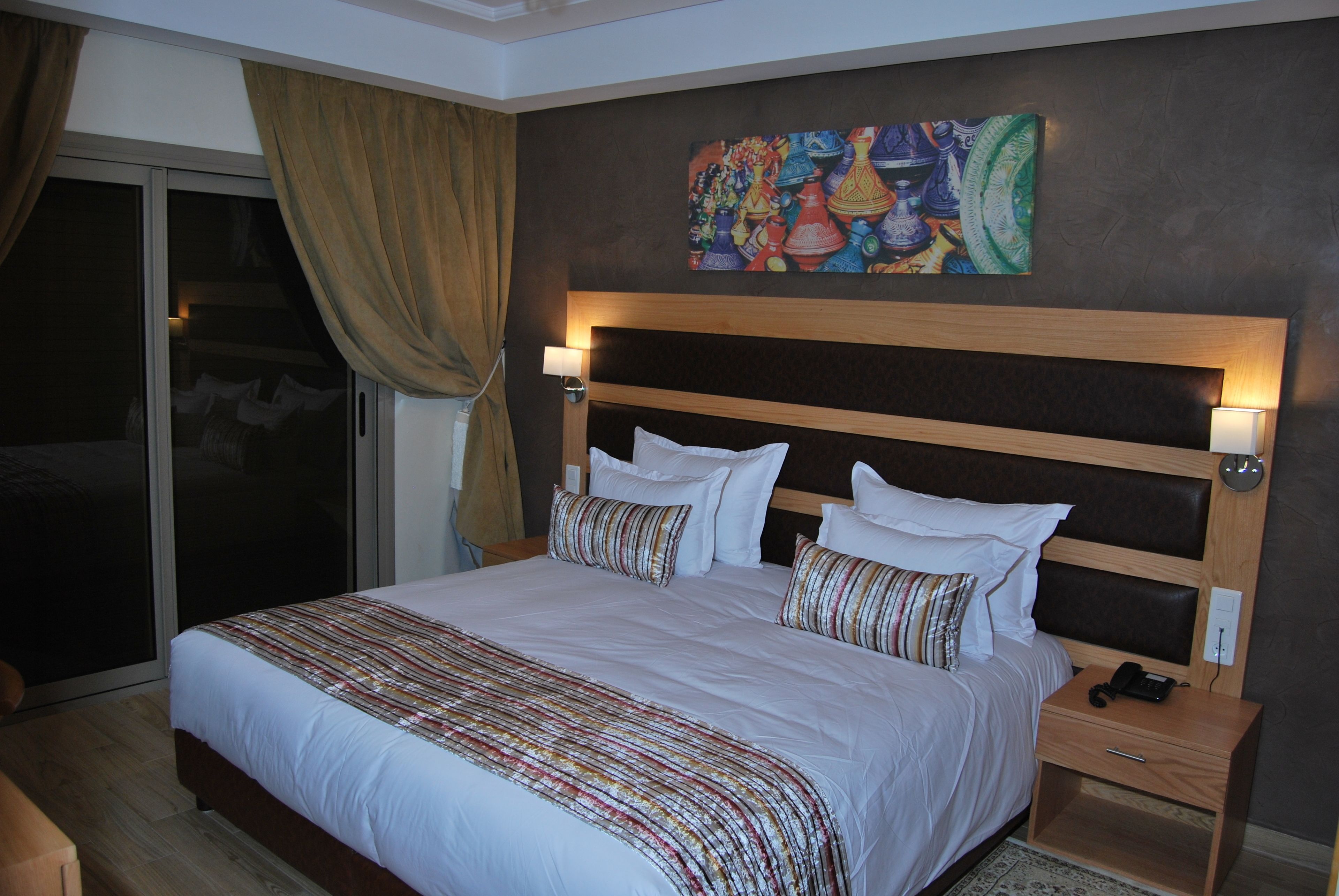 A hotel room with a large bed, a wooden headboard, two bedside lamps, and a colorful artwork on the wall.
