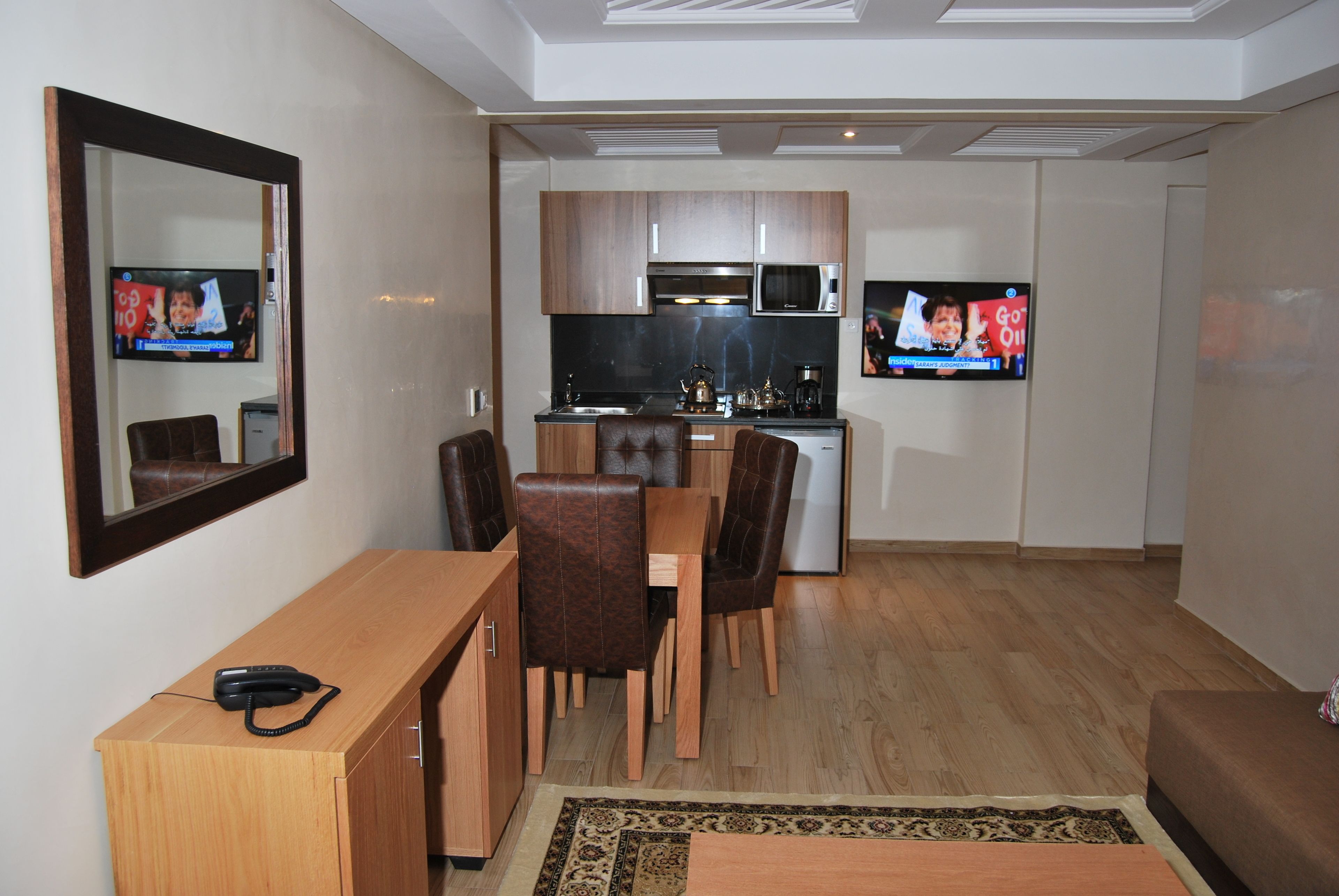A compact living space with a dining area, kitchenette, and a TV mounted on the wall.